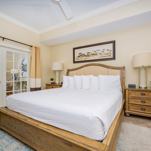 The master bedroom features a large king bed with plush pillows, a stylish lamp, and a view to the dining area