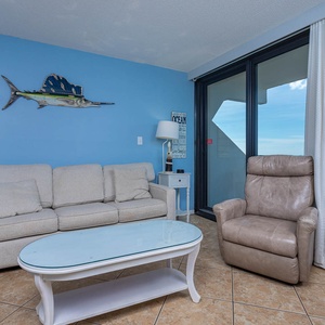 The living room features a nautical theme with comfortable furniture and large windows offering stunning beach views
