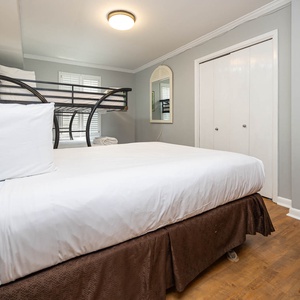 Cozy guest bedroom featuring a queen bed and a full bunk bed, with light gray walls and a mirror reflecting a welcoming vibe