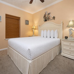 Cozy guest bedroom featuring a queen bed with plush white linens, bedside lamps, and beach decor on warm peach walls