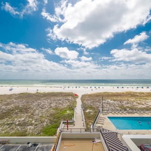 Stunning view of the pristine beach and inviting pool area under a bright blue sky, perfect for relaxation and fun