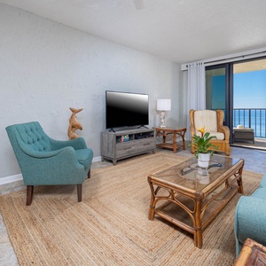This welcoming living space features a vibrant teal sofa, a large TV, and breathtaking views from the balcony