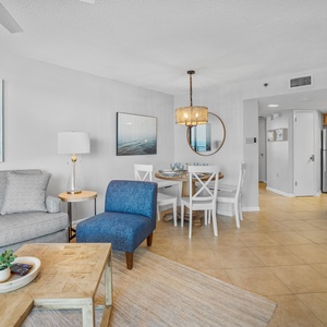 The open living area features a gray sofa, blue accent chair, and a dining table, creating a relaxed and inviting atmosphere