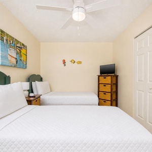 This cozy bedroom features two comfortable beds, a flat-screen TV, and cheerful nautical decor for a relaxing stay
