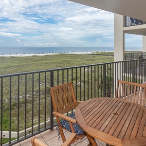Relax on the balcony with a table and chairs, overlooking the beach and vibrant blue umbrellas lining the shore