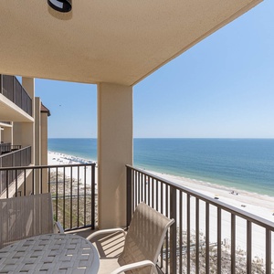 Balcony features a table and chairs, offering a serene view of the beach and sparkling blue water below