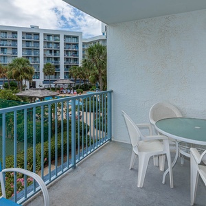 Enjoy a relaxing moment on the balcony with a view of the lush pool area, surrounded by palm trees and vibrant greenery