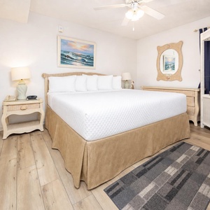 Bright and airy bedroom featuring a king bed, coastal decor, and a TV with a charming wicker dresser and mirror