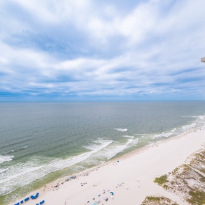 Breathtaking coastal view from a balcony, showcasing soft sands and gentle waves under a serene, cloudy sky