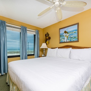 This bedroom features a large bed, soft blue curtains, and a beautiful beachfront view, perfect for relaxation