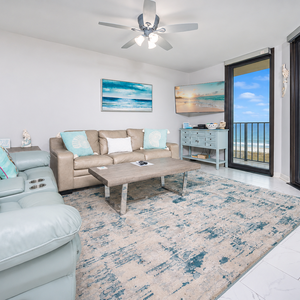 Cozy living area features a light blue sofa, decorative pillows, and a view of the beach through large sliding glass doors