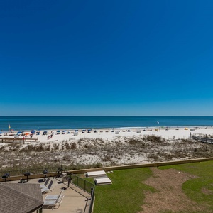 A serene view showcases the beach with white sand, colorful umbrellas, and a clear blue sky from the balcony