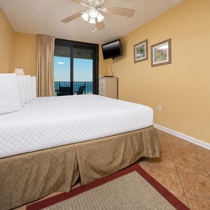 Spacious master bedroom with a king bed, light yellow walls, and a balcony view of the beach, perfect for relaxation