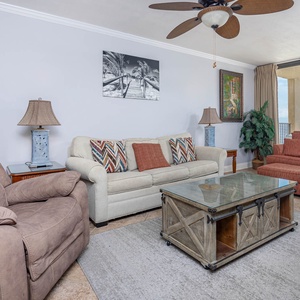The living area features a light-colored sofa with queen sleeper, a cozy armchair, and a glass-top coffee table