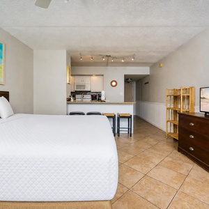 Efficiency suite featuring a plush king bed, kitchen area, and a vibrant beach-themed painting for a relaxing getaway