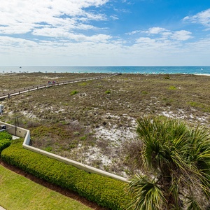 Expansive view of the beach with gentle waves, framed by grassy dunes and a pathway leading to the shoreline