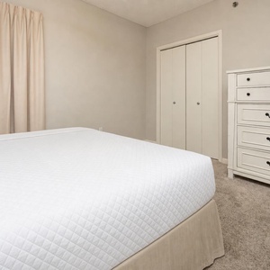 Guest bedroom featuring a queen bed, soft beige curtains, and a stylish dresser against a neutral wall