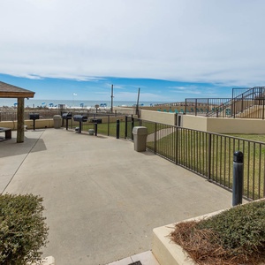 The outdoor area features a shaded gazebo with picnic tables, leading to a view of the beach and grassy space
