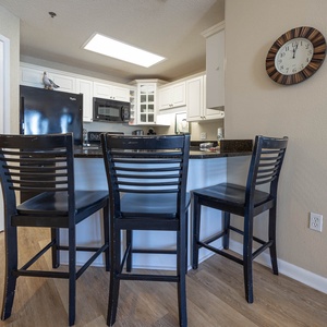 Black bar stools line the breakfast bar, overlooking a modern kitchen with white cabinetry and granite countertops