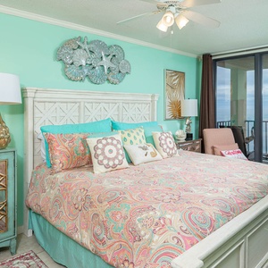 Brightly decorated master bedroom featuring a king bed, coastal accents, and a view of the beachfront balcony