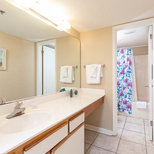 The master bathroom featuring a spacious vanity with a large mirror, colorful floral shower curtain, and fresh towels