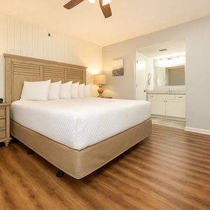 Master suite featuring a king bed with plush pillows, a wooden nightstand with a lamp, and an adjoining bathroom