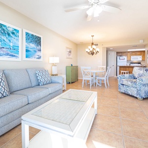 Bright living area features a comfortable sofa with decorative pillows, a dining table, and a cozy chair