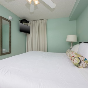Relax in this serene bedroom featuring a king bed, a mounted TV, and calming teal walls for a restful retreat