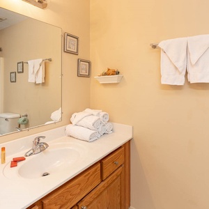 The guest bathroom features a clean, bright vanity with neatly stacked towels, a large mirror, and a tub/shower combo