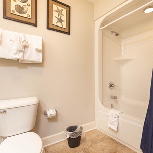 This guest bath features a clean design with coastal art, plush towels, and a shower/tub combo for a refreshing experience