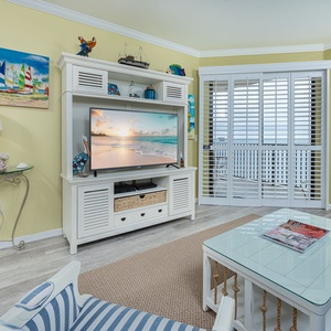 Brightly colored decor complements the living area featuring a large TV, comfortable seating, and access to a stunning beach