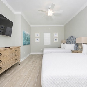 Relax in this guest bedroom featuring two comfortable queen beds, coastal decor, and a large TV