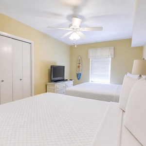 This guest bedroom features two queen beds, a TV, and a cheerful yellow wall, creating a bright and welcoming atmosphere
