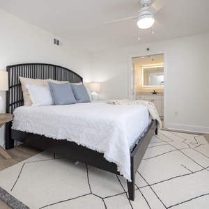 Master featuring a king bed with decorative pillows, a stylish lamp, and an adjoining bathroom visible in the background