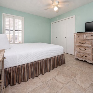 This cozy guest bedroom features a queen bed, a rustic dresser, and a TV, all set against a soothing mint green backdrop