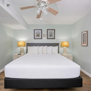 Plush king bed rests under a ceiling fan while soft lamps create a peaceful vacation suite glow