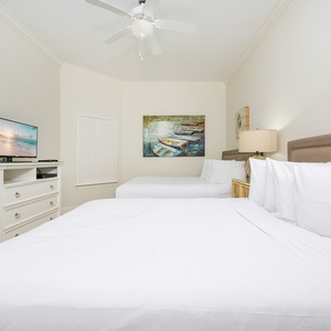 Inviting guest bedroom with two comfy queen beds, a TV, and beach-themed artwork for a relaxing getaway