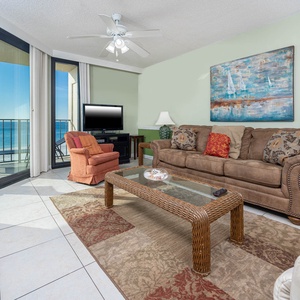 The living area features a comfortable brown sofa with queen sleeper, a vibrant orange chair, and a view of the beach