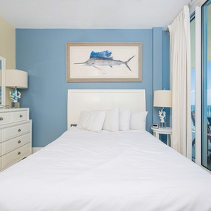 This guest bedroom features a serene blue accent wall, a comfortable bed, and a stunning beach view from the large windows