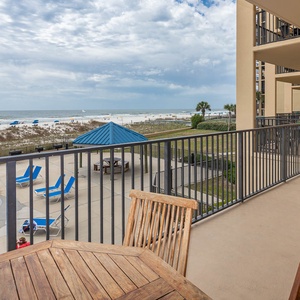 Enjoy a relaxing view from the balcony overlooking the beach, pool area, and lounge chairs under blue umbrellas