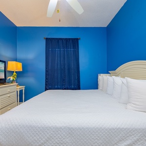 This bedroom features a large white bed, a TV for entertainment, and vibrant blue walls for a refreshing atmosphere