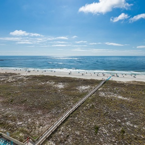 Expansive view of the beach with white sand, inviting turquoise waters, and a wooden boardwalk leading to the shoreline