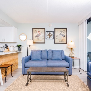 This inviting living area features a comfortable blue sofa, stylish decor, and a stunning beachfront view through large windows