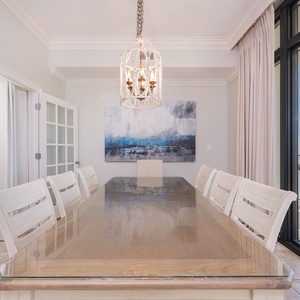 Dining area featuring a large table, elegant chandelier, and a stunning view of the coastline through glass doors