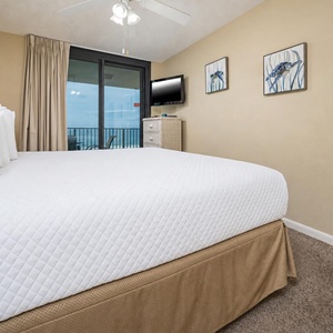 Inviting master bedroom features a plush king bed, wall-mounted TV, and access to a balcony with a serene beach view