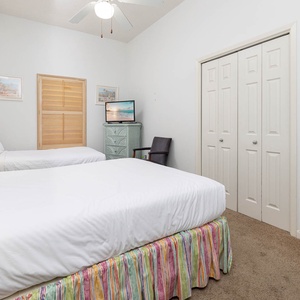 Guest room featuring two double beds with colorful skirts, a TV, and a cozy chair, providing a relaxed vibe for vacationers