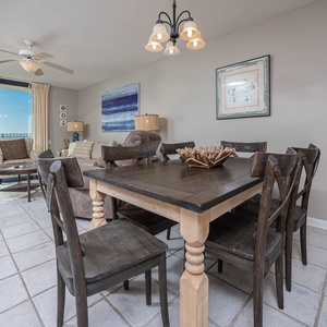 Dining area features a rustic wooden table with six chairs, complemented by a cozy seating nook and views of the beach