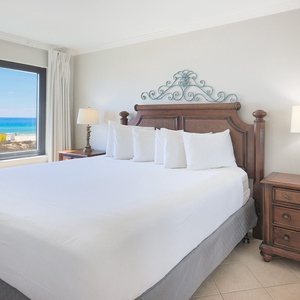 The master bedroom features a plush bed and stunning beachfront views through large windows