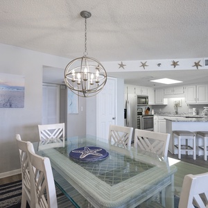 Dining area features a glass table with a starfish centerpiece, leading into a modern kitchen with bar seating