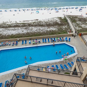 The pool area features a large blue pool with lounge chairs, while the beach is visible beyond the white sand